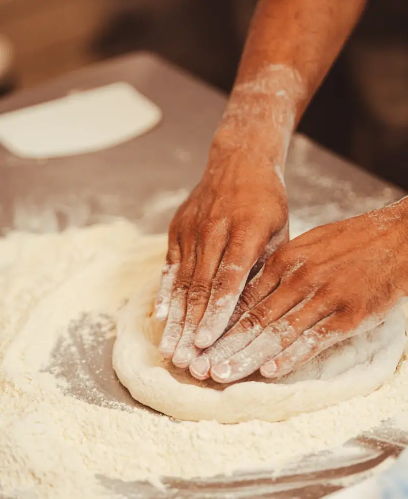 Mâini care întind aluat de pizza pe o masă presărată cu făină